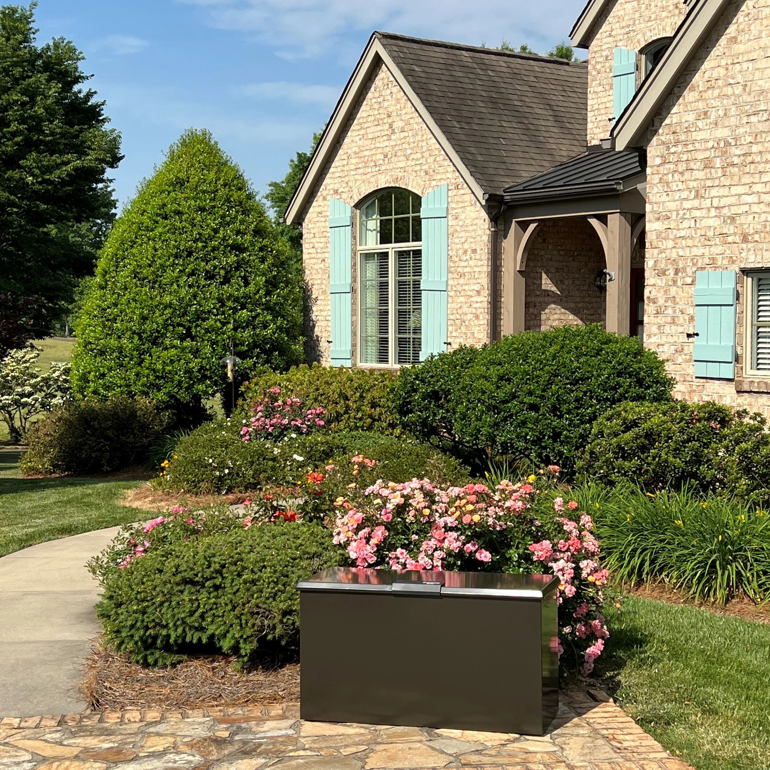 Brick house with green shutters and a well-maintained garden with flowers and shrubs with Brown Loxx Boxx