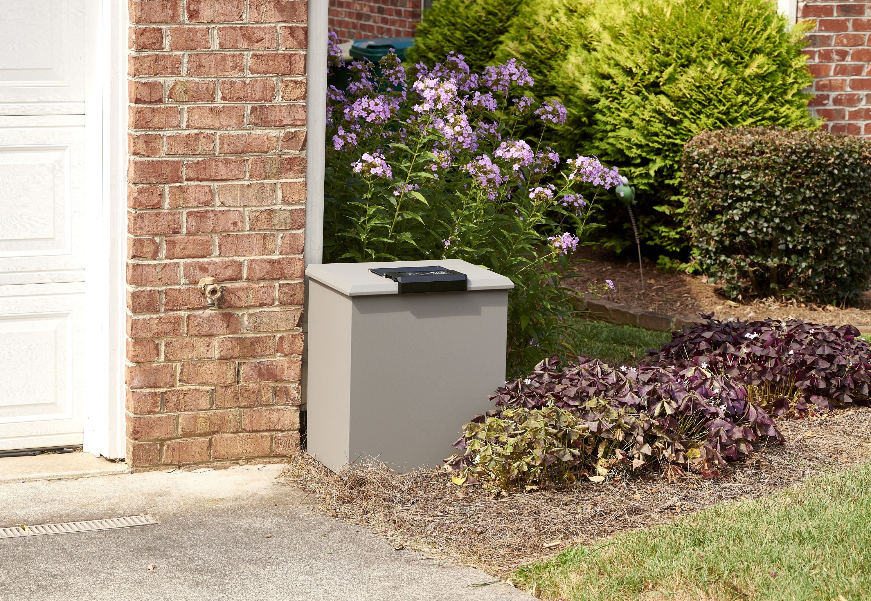 Outdoor Loxx Boxx against a brick wall with plants and flowers in the background